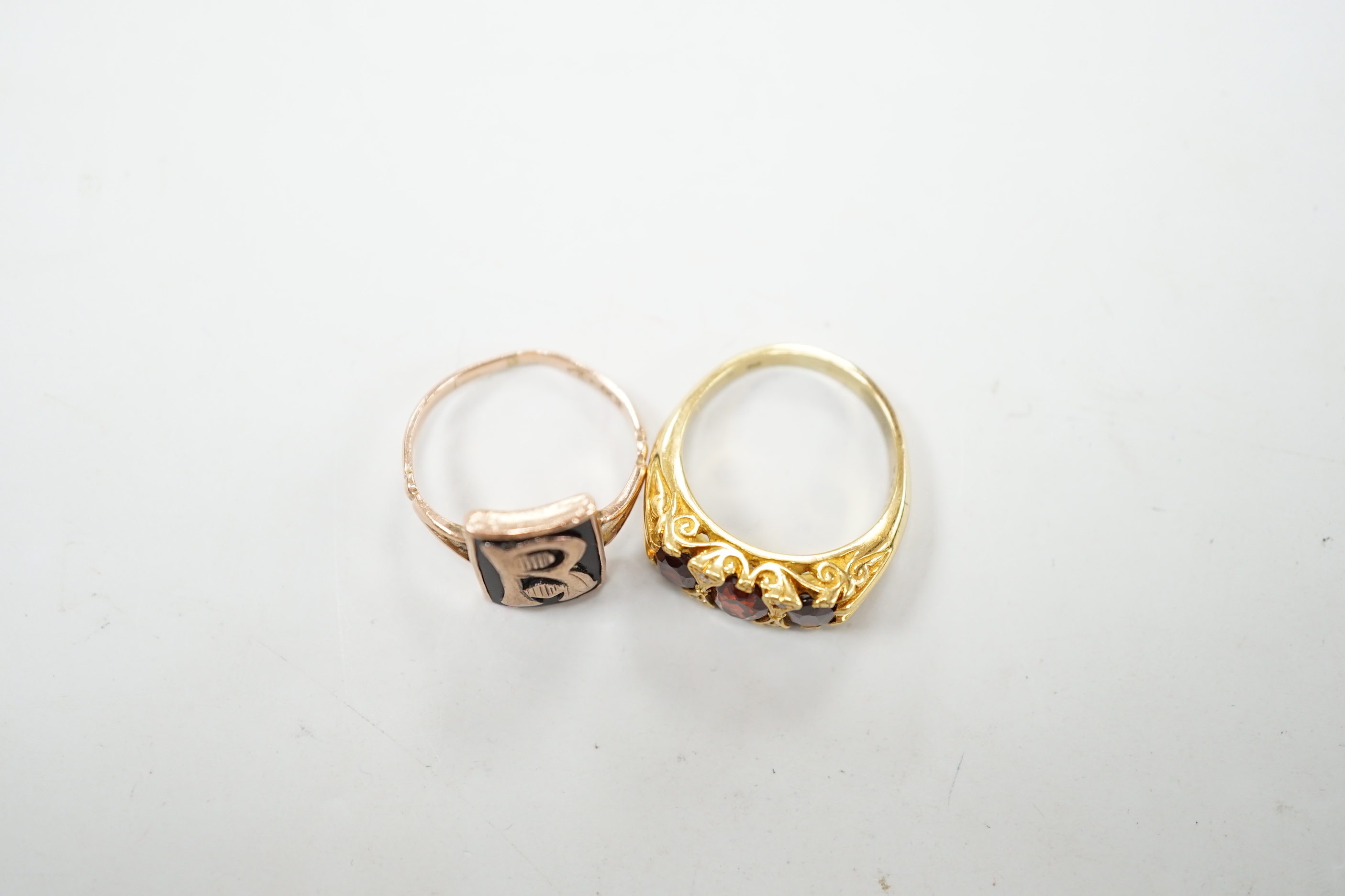 A yellow metal and three stone garnet set ring, with diamond chip spacers and a 9ct and black enamel set initial ring, gross weight 10.1 grams.